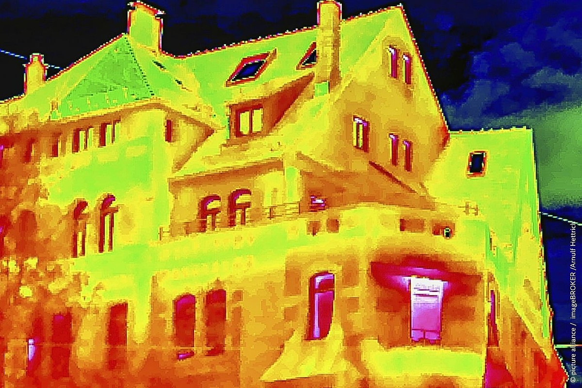 Thermal imaging scan of a multi-storey residential building, showing heat loss through walls, windows, and roof in a false-colour infrared palette ranging from cool blue (sky, well-insulated areas) to warm yellow-green (walls) to hot red-pink (windows and doorways where heat escapes most intensely)