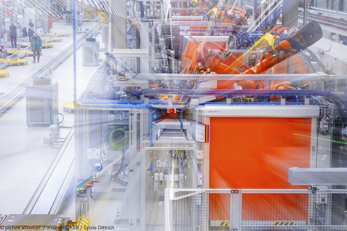 Automated production line with orange industrial robots in a modern European manufacturing facility, illustrating high-tech automotive or battery component assembly.