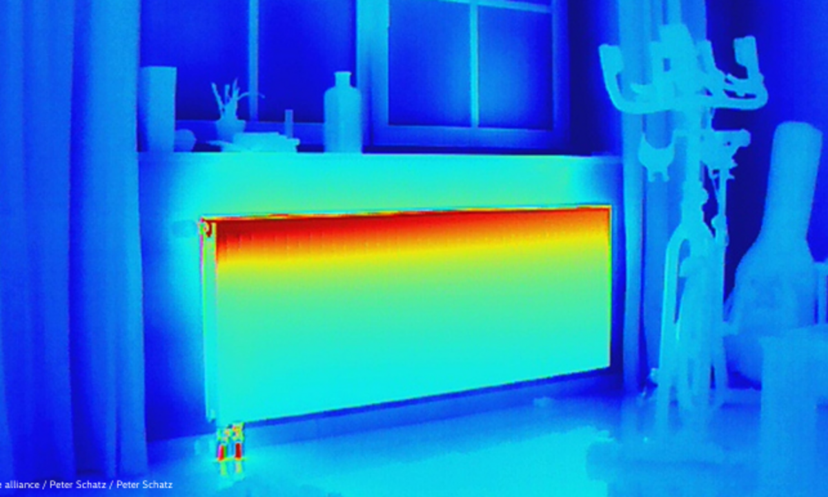 "Thermal image of an interior room showing heat loss through a radiator. The radiator displays a gradient from red-orange (hottest) at the top to yellow-green (cooler) below, while surrounding walls and furniture appear in blue tones (coldest), indicating significant temperature differences and potential energy inefficiency."