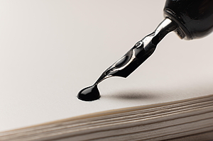 Eine Makroaufnahme eines Tintentropfens auf einem Notizblock. Ein Füllfederhalter ist in der Nähe. Retro-Bürokonzept.