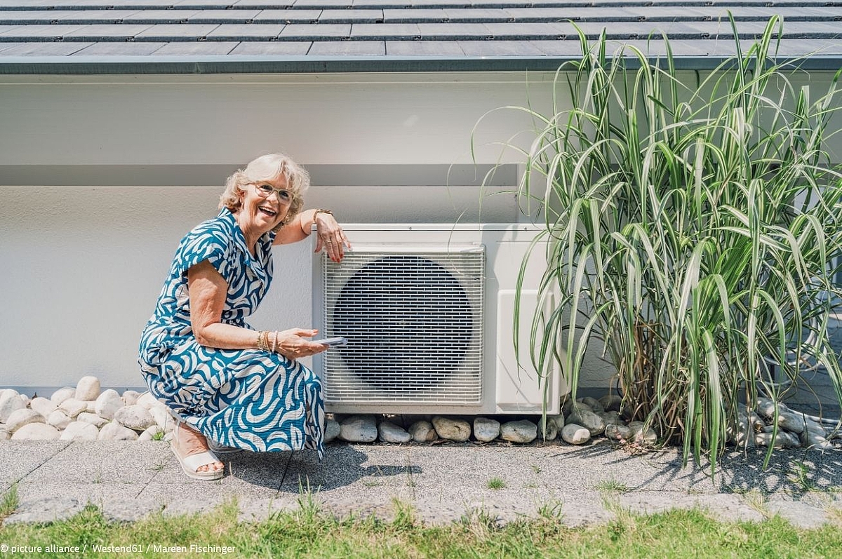 Smiling woman adjusting heat pump with smartphone in home garden